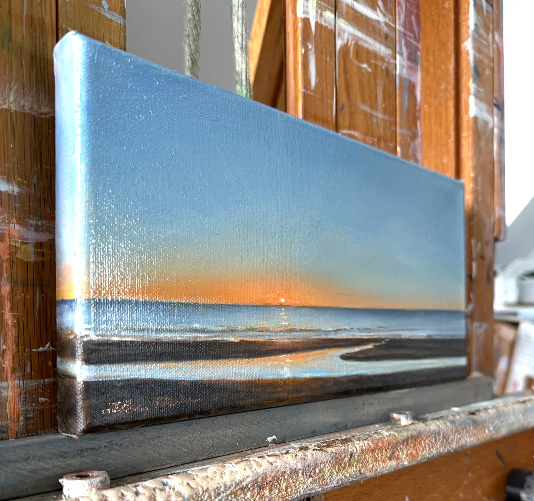 A radiant painting of the sun rising over the ocean, the sky gradually going from blazing on the horizon to deep blues, all reflected in a tidal pool in the foreground sand.